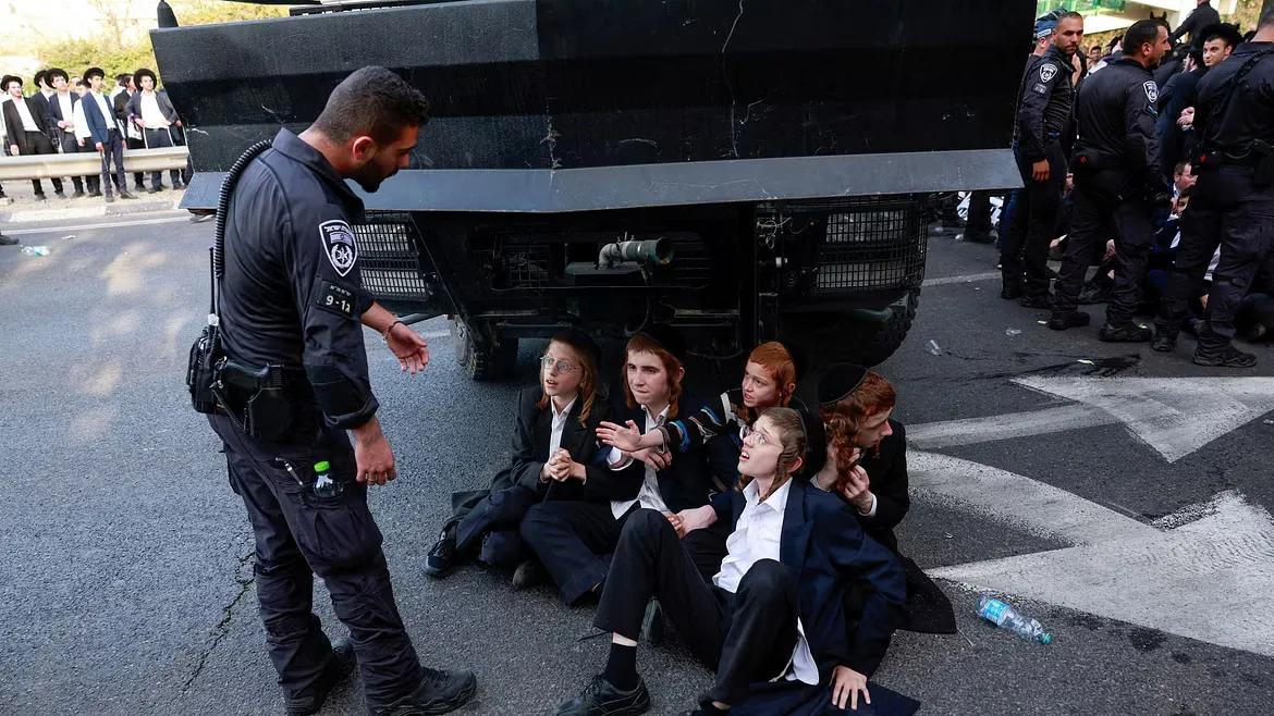 Ultra-Orthodox Jewish demonstrators sit on the street next to a police officer